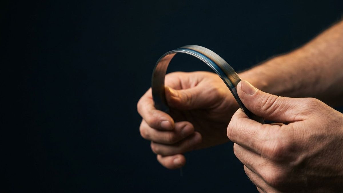 Two hands bending a strip of spring steel against a dark background